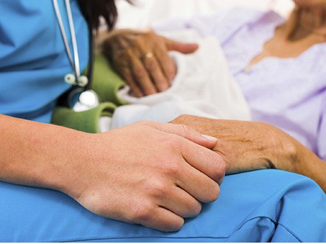 A caregiver holds a hand of a patient in a hospital bed